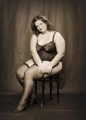 Fototapeta na wymiar Overweight woman dressed in corset and folding fan. Black and white sepia filtered photography. Vintage style picture on fashion theme.