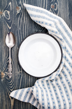 Empty White Enamel Plate Wrapped with Napkin on Wooden Backgroumd