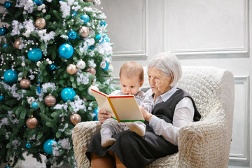 Senior woman reading a book to her great grandson while sitting beside a Christmas tree