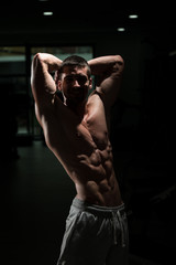 Fototapeta na wymiar Muscular Man Flexing Muscles In Dark Gym