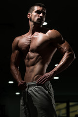 Fototapeta na wymiar Muscular Man Flexing Muscles In Dark Gym
