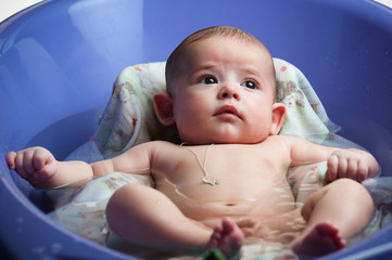 Baby bathing in a purple bathtub at home.