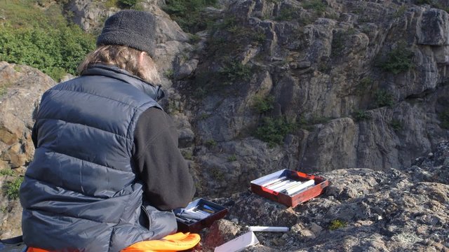 Expeditioner drawing while sitting at a small waterfall in Torngat Mountains.