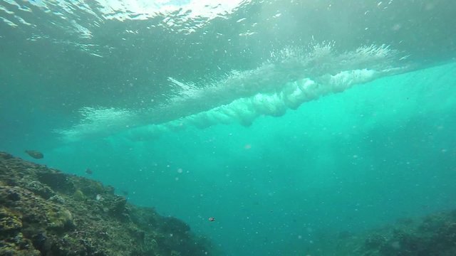 Surfing wave breaking over coral reef, slow motion underwater view 