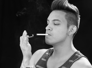 Fototapeta premium Hispanic male headshot posing with serious facial expression and smoking a cigarette smoke visible, black white edition