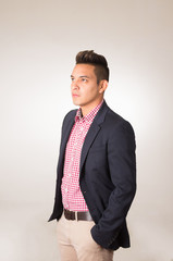 Hispanic male wearing shirt and blazer jacket standing with hands in jeans pocket empty background