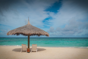 Straw parasol sunshade and sun loungers on a tropical beach in the Maldives
