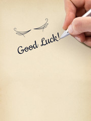 Hand writing "Good Luck!" on aged sheet of paper.