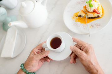 Old woman hands hold a cup of coffee on marble table with a piec