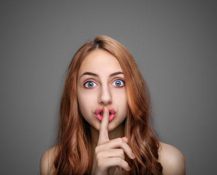 Girl  keeping finger on her lips , isolated on gray.