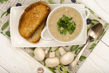 Mushroom cream soup  with roasted bread on the white wooden surface.