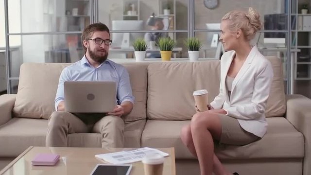 Man showing funny picture on his laptop to colleague and she laughing at it
