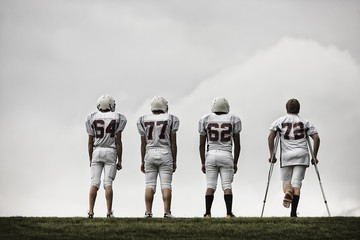 American football players standing in field, one using crutches