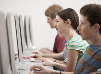 A group of young people, boys and girls, students in a computer class working at screens. 