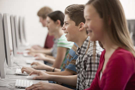 A group of young people, boys and girls, students in a computer class working at screens. 