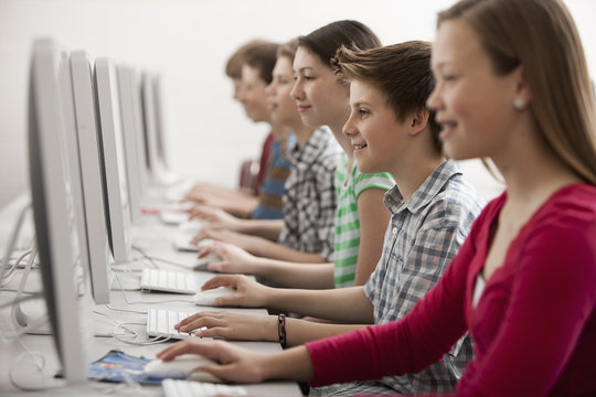 A group of young people, boys and girls, working at computer screens in class. 