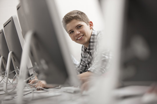 A school room, computer laboratory or lab with rows of computer monitors and seating. A young person seated working at a terminal.