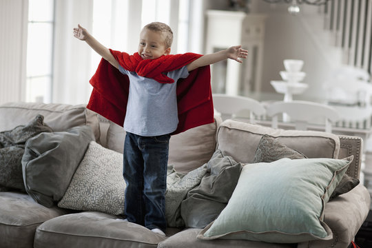 A child standing wearing a red cape, arms raised in a  superhero pose. 