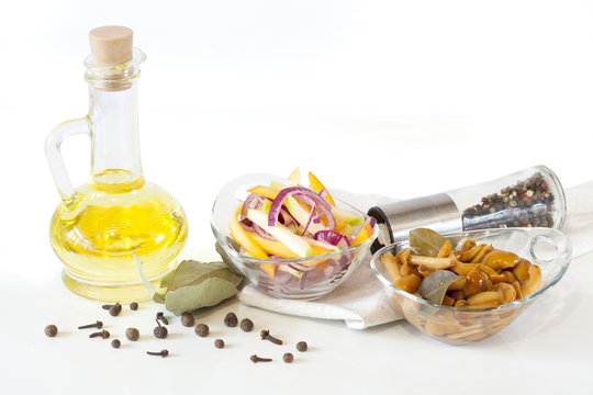 Olive oil, delicious marinated mushrooms and salad with fresh onion and vegetables in glass plate in glass bowls on white background