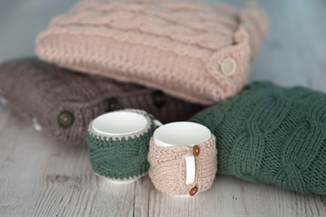 Obraz na płótnie Canvas three knitted pillows and two cups on wooden board background
