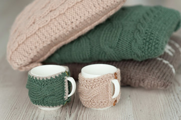 Fototapeta na wymiar three knitted pillows and two cups on wooden board background
