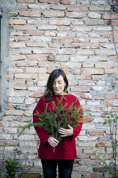 A woman holding in her arms pine branches for to make a christmas garland in front of a brick wall