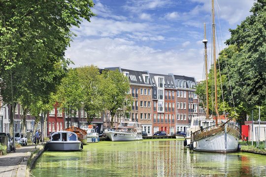Green canal with moored yachts and apartment buildings, Gouda, Netherlands.