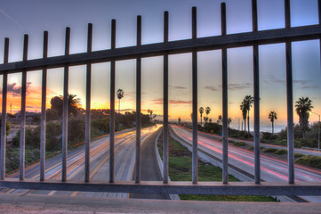 Freeway traffic shows through iron bars. 