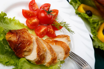 Sliced roasted chicken breast and served with fresh vegetables on white plate close up