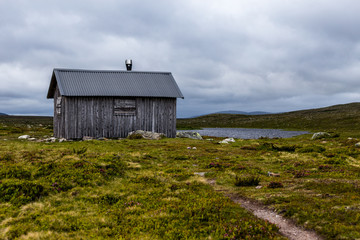 Obraz premium Old grey wooden house on prairie, much clouds Mountain in backgraound