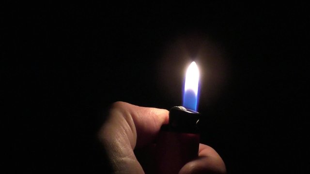 Strike a lighter to light a fire in the dark flame gas lighter