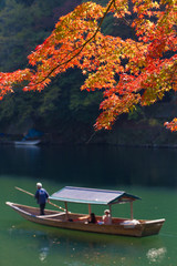 Arashiyama, red maple leaves blooming at Arashiyama in Autumn with tourists in a boat service rowing in Katsura river with nice scenery, Kyoto, Japan