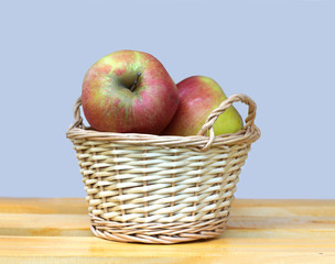 BIg ripe red and yellow apples in light brown wicker basket on wooden table against gray background closeup