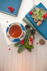 A cup of tea/A cup of black tea, books and coniferous winter composition with pine cones and rowan. Light background