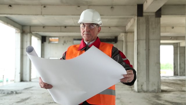 Worker in white hard hat with building drawings at project site. Manager of the works at construction site