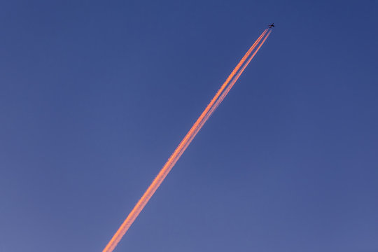 Airplane With Contrail High In The Sky At Sunset