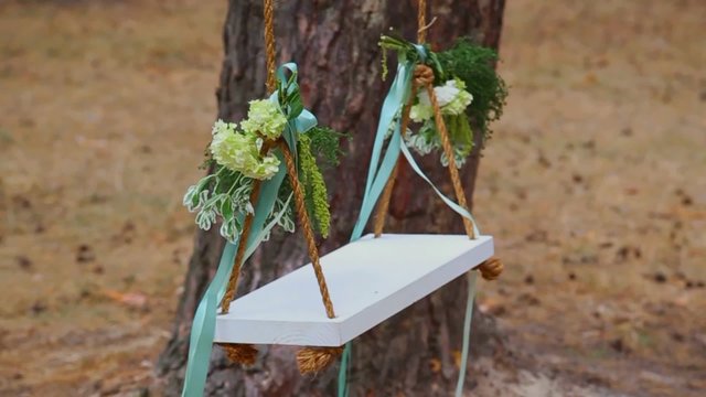 Beautiful wood swing hanged on a tree at forest background. Swing decorated with bouquets of flowers