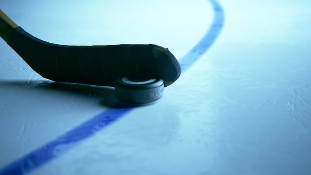 Hockey Stick shoots a black rubber puck on a rink arena from marking line.