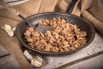 Cooking Ground sausage meat in frying pan with garlic and burlap background