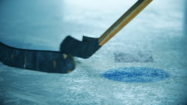Two Ice Hockey Sticks fighting for a rubber puck on ice hockey rink arena.
