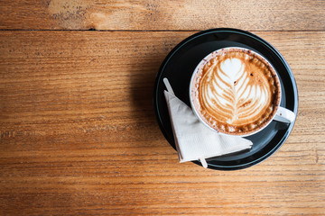 A cup of cappucino and a napkin on a wood background - obrazy, fototapety, plakaty
