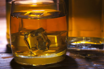 Glass of whiskey with ice on a wooden background