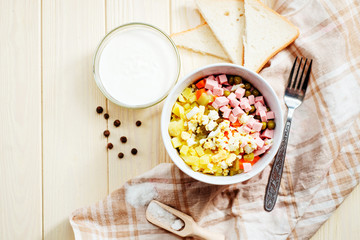 
Russian salad with potatoes , sausage , carrot , egg and green peas , mayonnaise or sour cream and spices on a wooden background