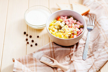 
Russian salad with potatoes , sausage , carrot , egg and green peas , mayonnaise or sour cream and spices on a wooden background