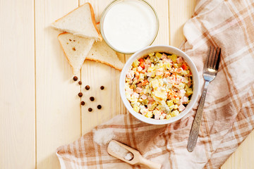 
Russian salad with potatoes , sausage , carrot , egg and green peas , mayonnaise or sour cream and spices on a wooden background