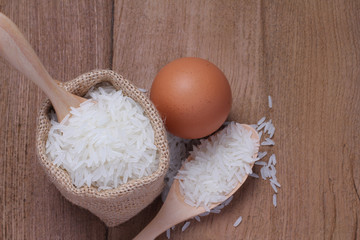 White rice in small burlap sack and eggs with rice straw on wooden background