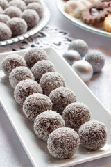 Christmas coconut balls  on a white plate. Mixed sugar cookies in the background.
