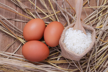 White rice in small burlap sack and eggs with rice straw on wooden background