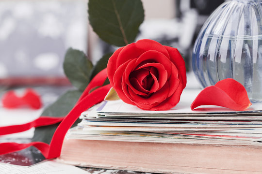 Red rose flower with a stack of postcard, retro photos and vintage book