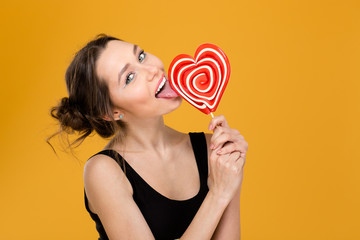 Lovely playful woman licking sweet heart shaped lollipop